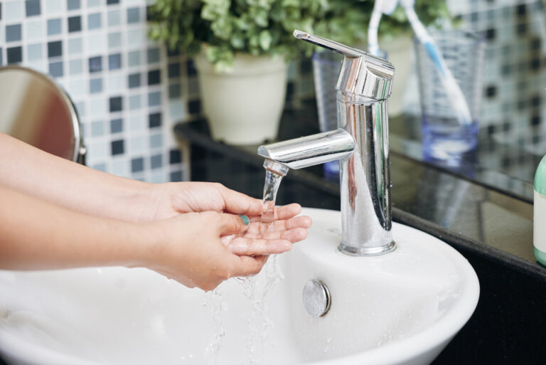 Crop woman washing hands in bathroom